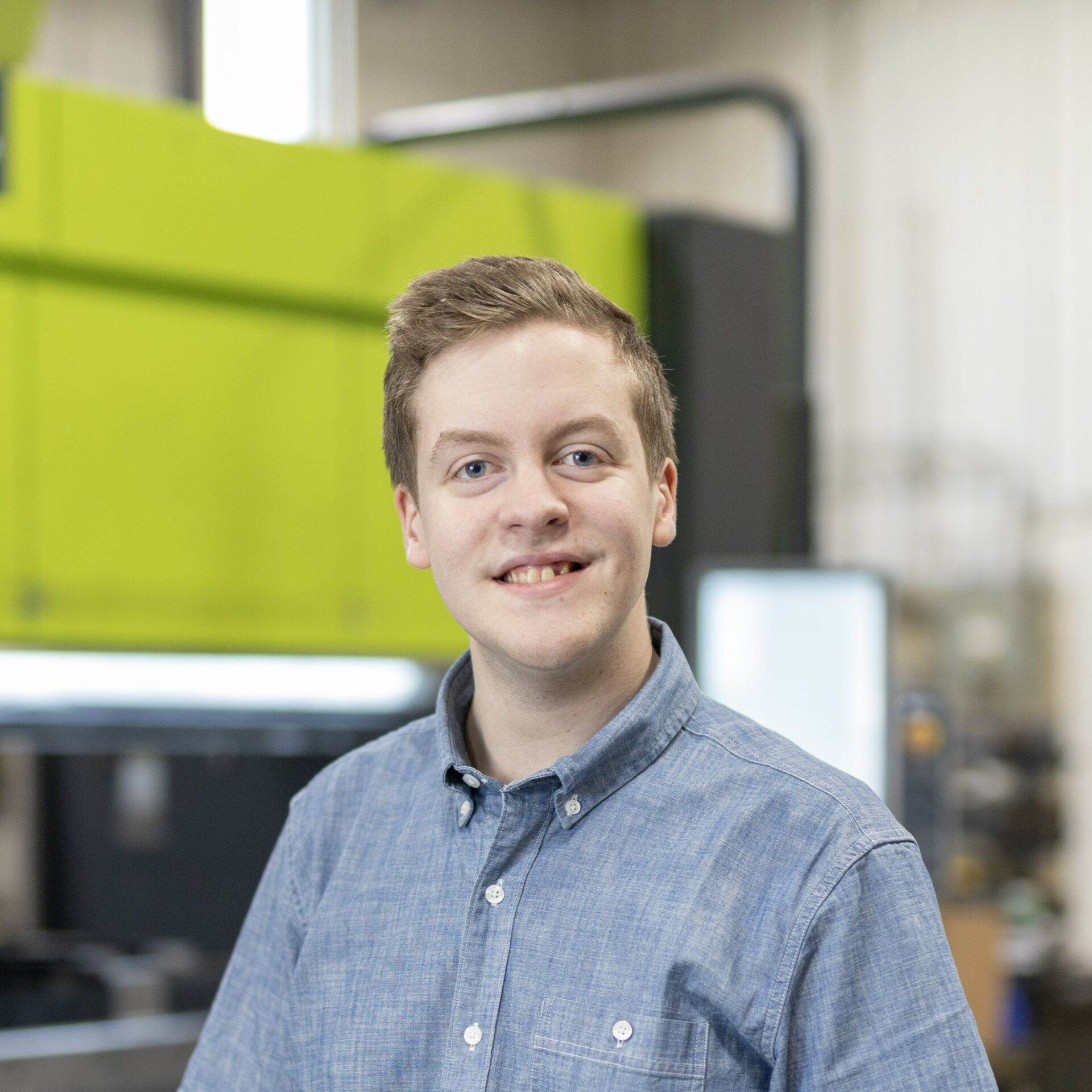 A man in a blue shirt standing in front of a metal fabrication machine.
